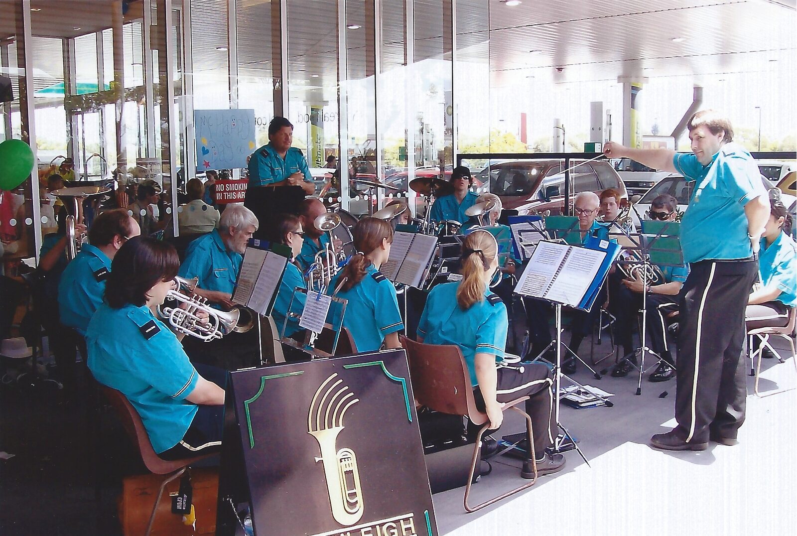 Beenleigh Brass Band playing at an outdoor event with the conductor standing